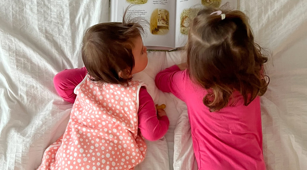 Két kislány rózsaszín pizsamában hasal az ágyon és olvas