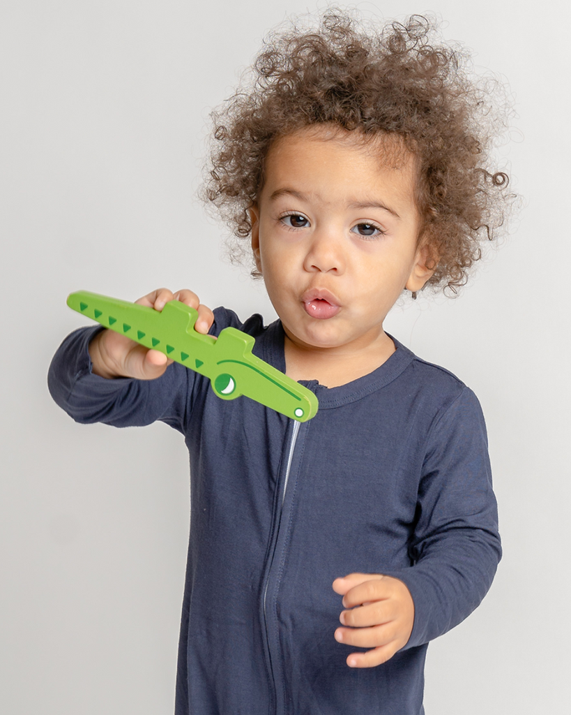Brown boy with curly hair wearing blue bamboo zip up sleepsuits while playing with a crocodile
