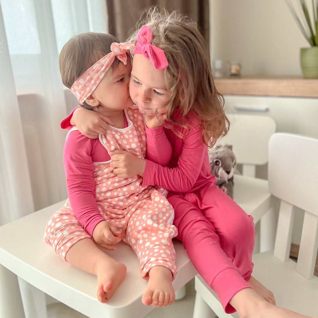 Két kislány az asztalon ülve rózsaszín pizsamában egymást ölelve