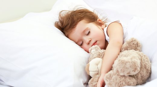 Kislány alszik fehér ágyban maciját ölelve