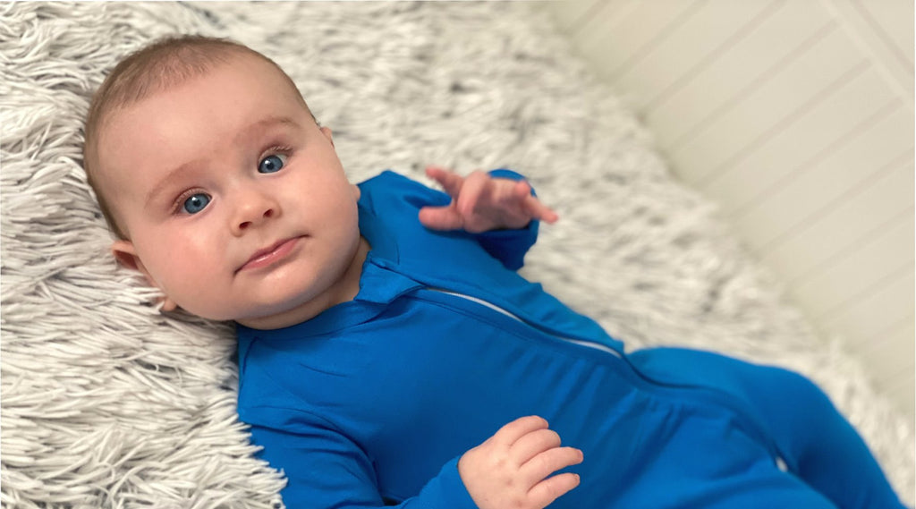 cute baby boy laying on his back smiling and wearing blue zip-up sleepsuit wiht feet