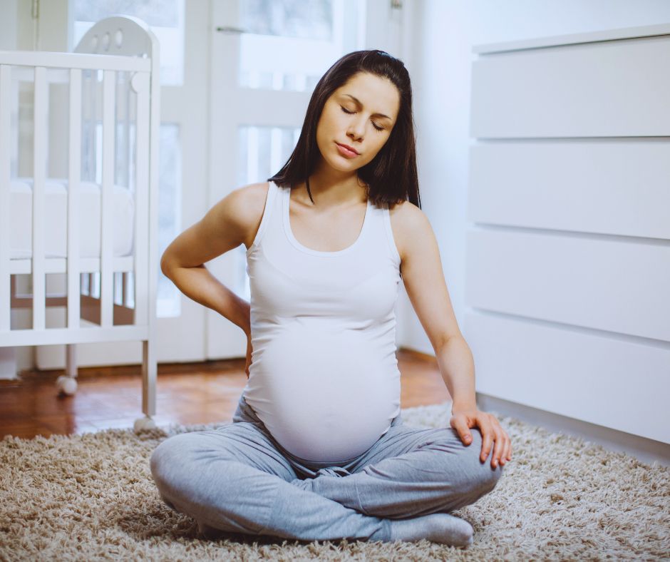 Kismama ül a földön és próbálja enyhíteni hátfájását