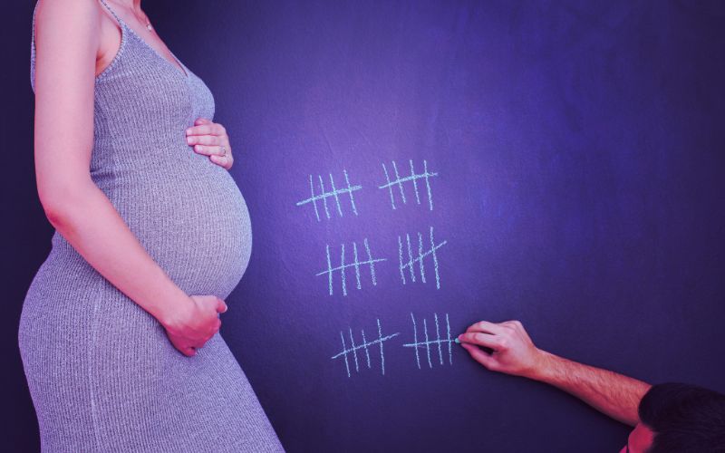 várandós kismama hasa és a terhességi heteket számláló vonalak egy táblán