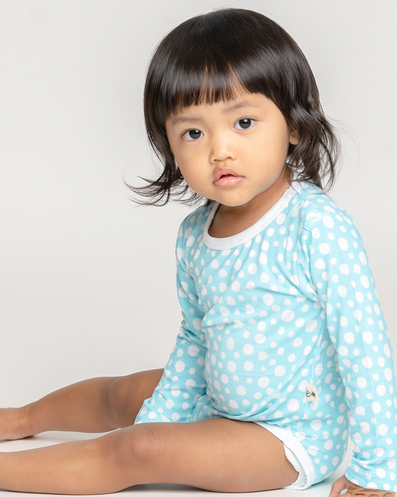 Ázsiai kislány ül - kék fehér pöttyös hosszú ujjú baba bodyt viseel