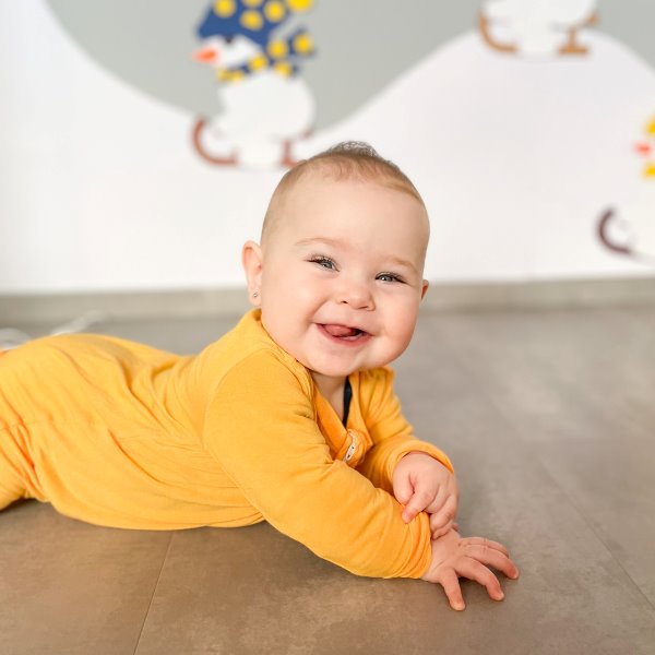 kislány baba hasal és mosolyog sárga rugdalózóban