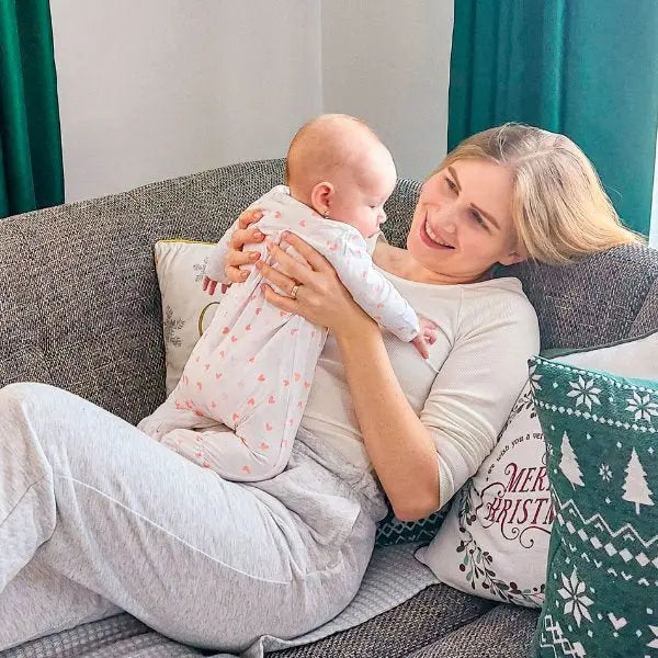 anyuka kanapén fekve kezében emeli kisbabáját szíves liaabebe rugdalózóban